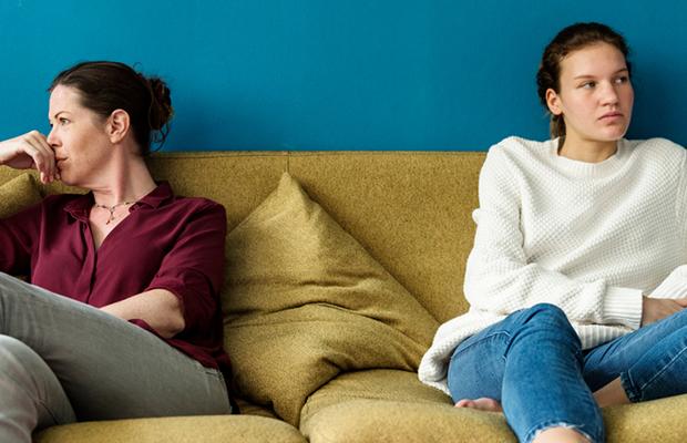 angry mom and teen girl sitting at either end of couch looking away from each other